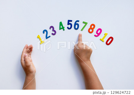 Child hands pointing at colorful wooden numbers on white background 129624722