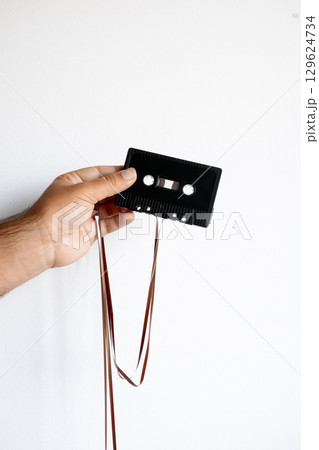 Hand holding vintage audio cassette with unwound tape 129624734