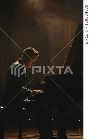 professinal pianist playing on piano at dark stage, man play at performance on grand piano instrument, back light and illumination 129624929