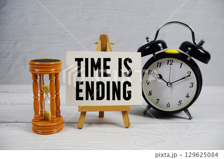 Time is Ending text with hourglass and alarm clock on wooden background Time is Ending text with hourglass and alarm clock on wooden background 129625084