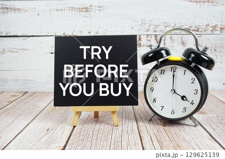 Try Before You Buy text with easel and alarm clock on wooden background 129625139