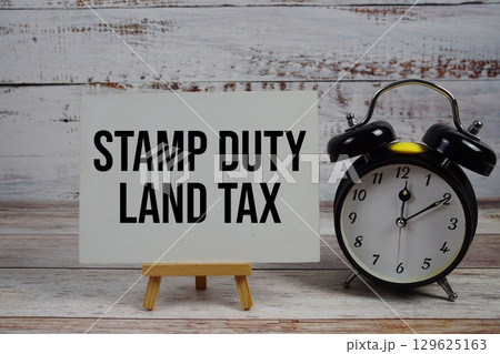 Stamp Duty Land Tax text with easel and alarm clock on wooden background Stamp Duty Land Tax text with easel and alarm clock on wooden background 129625163