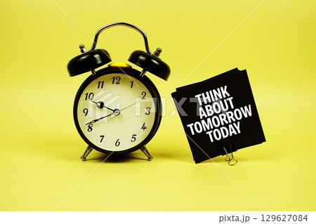 Think About Tomorrow Today text message on paper card with alarm clock on yellow background Think About Tomorrow Today text message on paper card with alarm clock on yellow background 129627084