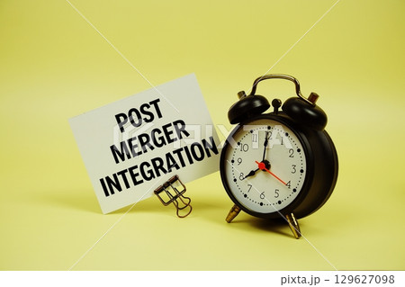 Post Merger Integration text message on paper card with alarm clock on yellow background 129627098