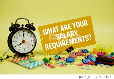 What are Your Salary Requirements? text on paper card with alarm clock and stationery on yellow background What are Your Salary Requirements? text on paper card with alarm clock and stationery on yellow background 129627107
