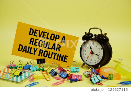 Develop A Regular Daily Routine text on paper card with stationery and alarm clock on yellow background 129627116