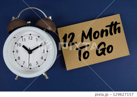 12 Month To Go text written on paper with alarm clock on blue background 129627157