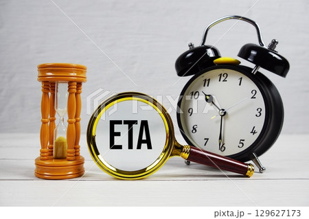 ETA abbreviation of Estimated Time Of Arrival text with alarm clock on wooden background 129627173