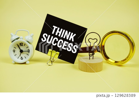 Think Success text message on sticky note with magnifying glass and alarm clock on yellow background 129628389