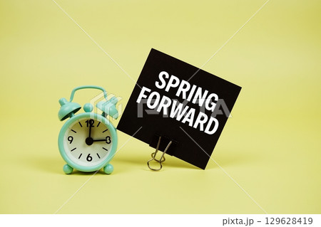Spring Forward text message on paper card with alarm clock on yellow background 129628419