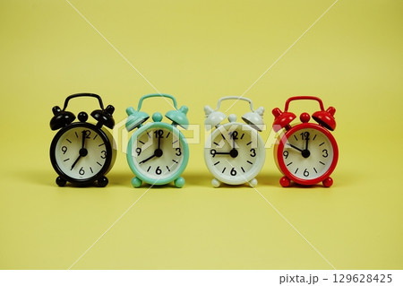 Alarm clocks with different time on yellow background Alarm clocks with different time on yellow background 129628425