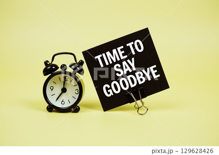 Time to say Goodbye text message on paper card with alarm clock on yellow background Time to say Goodbye text message on paper card with alarm clock on yellow background 129628426