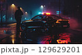 A police officer stands near patrol cars on a misty street at night, with blue and red lights reflecting on the wet road, creating a tense atmosphere of a potential crime scene 129629201