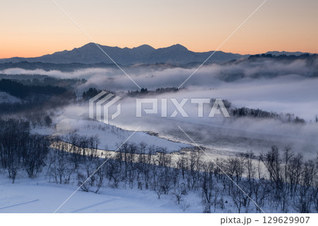 新潟県小千谷市　霧の流れる信濃川と朝焼けの越後三山の雪景色 129629907