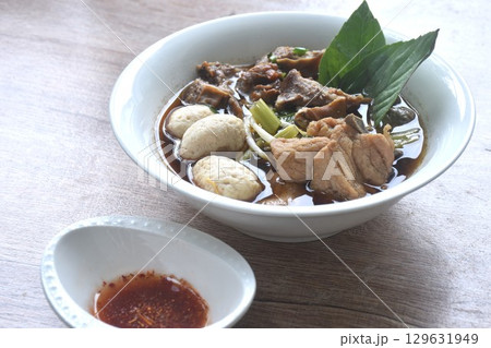 braised pork tendon and meatball with bean sprout toping fresh basil in brown soup on bowl dipping spicy sour chili sauce 129631949