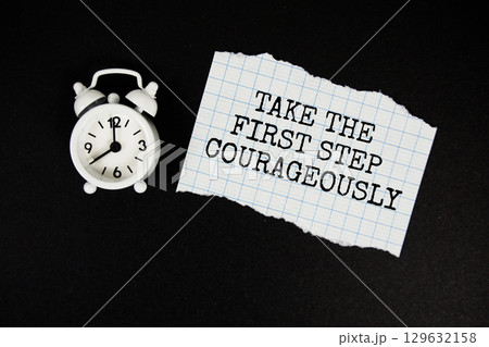 Take The First Step Courageously text written on paper with alarm clock on black background 129632158