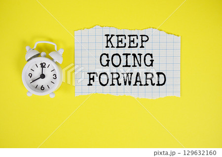 Keep Going Forward text written on paper with alarm clock on yellow background 129632160