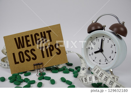 Weight Loss Tips text with medicine, alarm clock and measuring tape on white background Weight Loss Tips text with medicine, alarm clock and measuring tape on white background 129632180