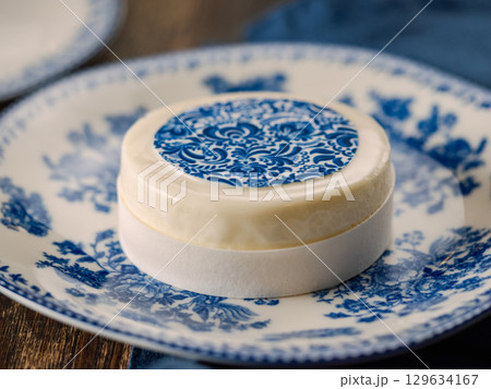 Pastry dessert in Gzhel rustic style. Sweet pastry decorated blue flowers photo printing on sugar paper. Mini cake Gzhel on plate over wooden tabletop background. Closeup Pastry dessert in Gzhel rustic style. Sweet pastry decorated blue flowers photo printing on sugar paper. Mini cake Gzhel on plate over wooden tabletop background. Closeup 129634167