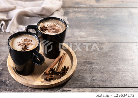 Chai Latte in Black Mug with Spices( star anise and cinnamon) on wooden table 129634172