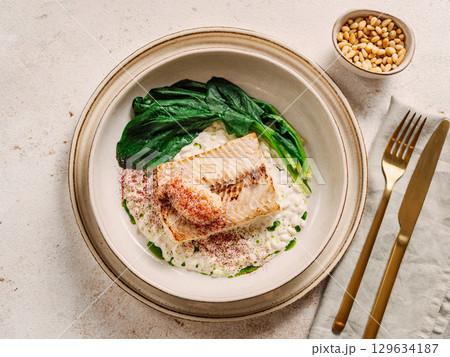 White fish on pillow of pine nut garnished with blanched spinach and white caviar, on restaurant table. Delicious dish with whitefish, top view White fish on pillow of pine nut garnished with blanched spinach and white caviar, on restaurant table. Delicious dish with whitefish, top view 129634187