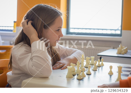 Clever schoolgirl playing chess game in school classroom. Child girl on chess lesson strategy 129634329