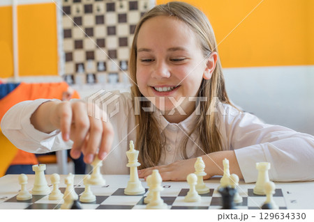 Happy schoolgirl playing chess game in school classroom. Child girl on chess lesson strategy 129634330