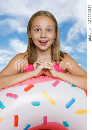 Happy little girl and colorful inflatable ring swimming float against blue sky Happy little girl and colorful inflatable ring swimming float against blue sky 129634336