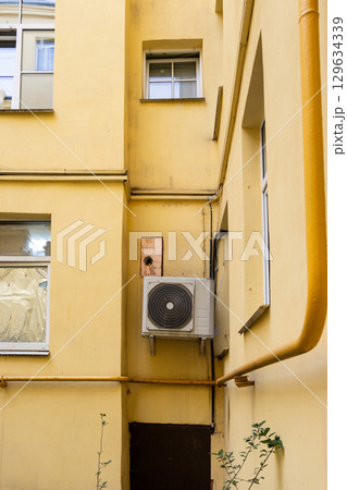 dirty air conditioner unit is mounted on a yellow wall. ventilation and cooling of the home. dirty air conditioner unit is mounted on a yellow wall. ventilation and cooling of the home. 129634339