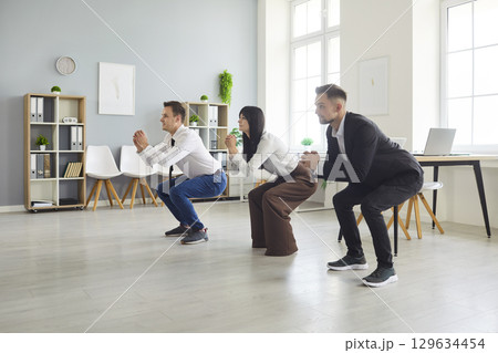 Business team doing synchronized squats together during an office fitness break 129634454