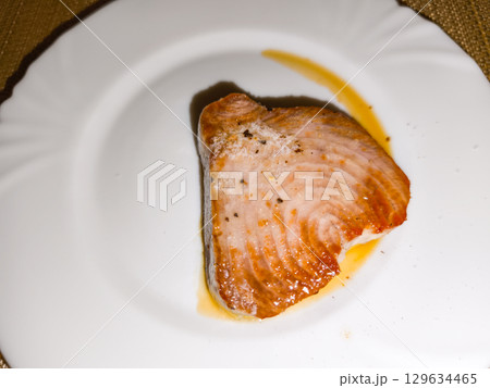 Grilled tuna steak with salt and pepper resting on white plate 129634465