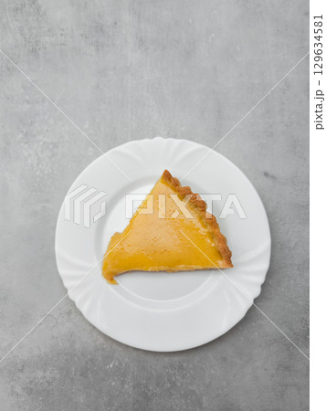 Delicious lemon tart slice sitting on white plate on gray table Delicious lemon tart slice sitting on white plate on gray table 129634581