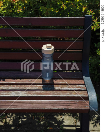 Reusable water bottle sitting on park bench promoting hydration and sustainability 129634600