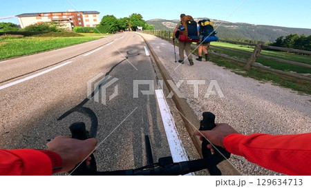 POV road cycling past backpacking tourists in mountain village, French Alps 129634713