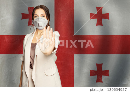 Confident woman in medical mask showing stop gesture open palm hand against flag of Georgia Confident woman in medical mask showing stop gesture open palm hand against flag of Georgia 129634927
