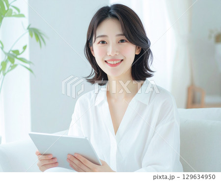 在宅勤務でタブレットを使う笑顔の若い女性 在宅勤務でタブレットを使う笑顔の若い女性 129634950