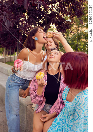 Young people playfully feeding each other donuts on park bench Young people playfully feeding each other donuts on park bench 129635134