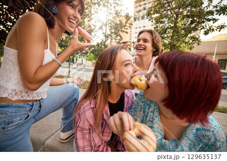 Friends sharing donuts and enjoying fun moments together on sunny day 129635137