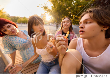 Young friends enjoying snacks on bench during golden hour city sunset 129635143