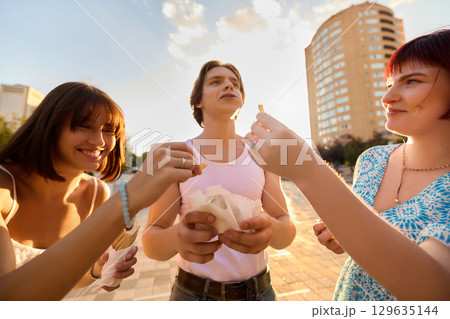 Friends sharing fries outdoors in warm sunset light with joyful expressions 129635144