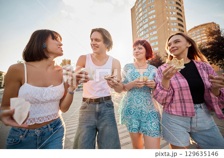 Young people walking in urban area laughing and eating fast food together 129635146