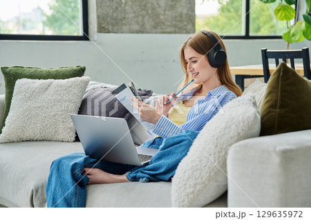 Young teen girl student in headphones with laptop textbook watching video lesson at home 129635972