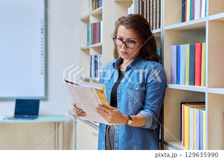 Portrait serious mature woman teacher, educational specialist reading textbook in classroom 129635990