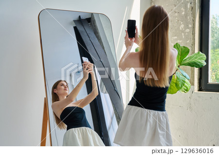 Smiling young teenage female taking selfie photo on smartphone 129636016