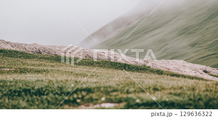 Fog envelops lush green hills on a serene landscape in early morning light Fog envelops lush green hills on a serene landscape in early morning light 129636322