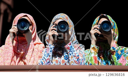 Three veiled women with floral hijabs holding cameras against a 129636816