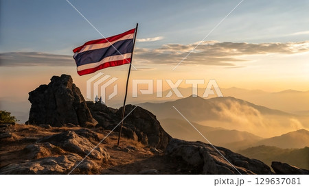Thai flag atop rocky peak overlooking misty mountain range at sunrise 129637081