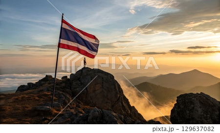 Person standing near thailand flag on rocky mountain during golden hour sky 129637082