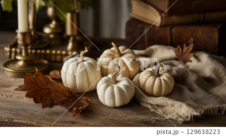 Rustic pumpkin arrangement with dried leaves, linen fabric and brass candlestick on wooden table in soft golden afternoon light for cozy Halloween decor 129638223