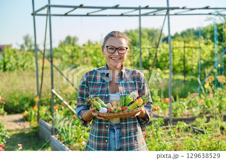 Portrait of woman showing basket with different fresh vegetables and herbs in garden 129638529